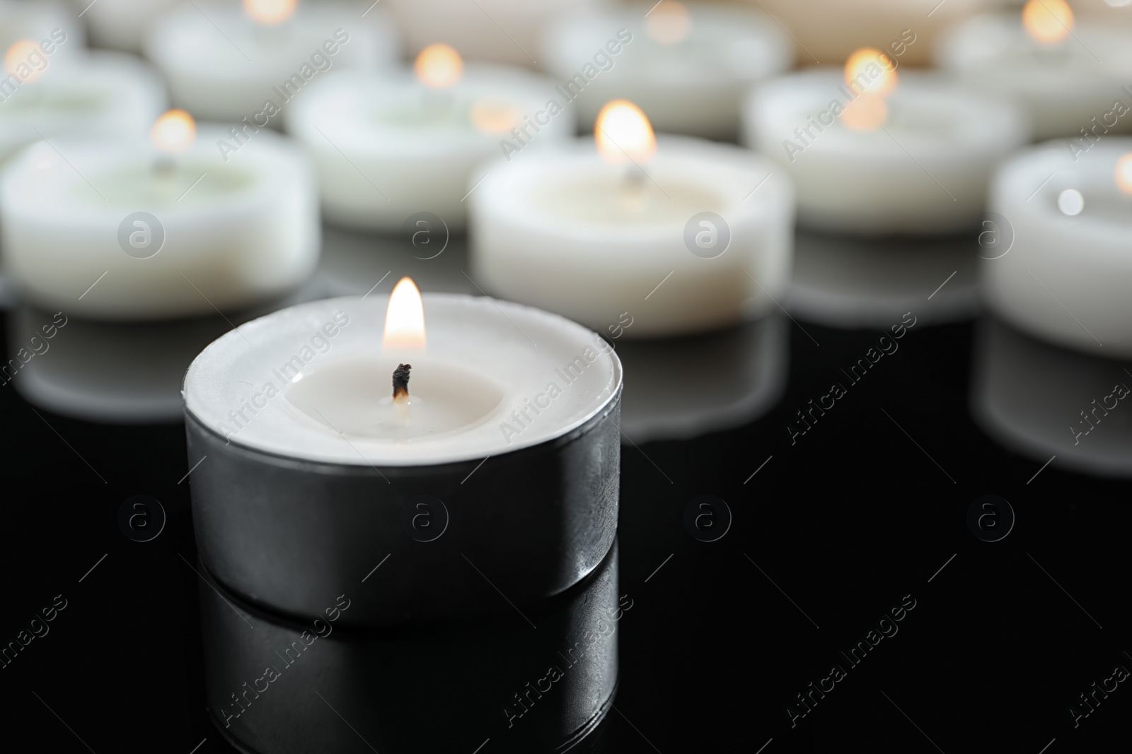 Photo of Wax candles burning on table in darkness, closeup