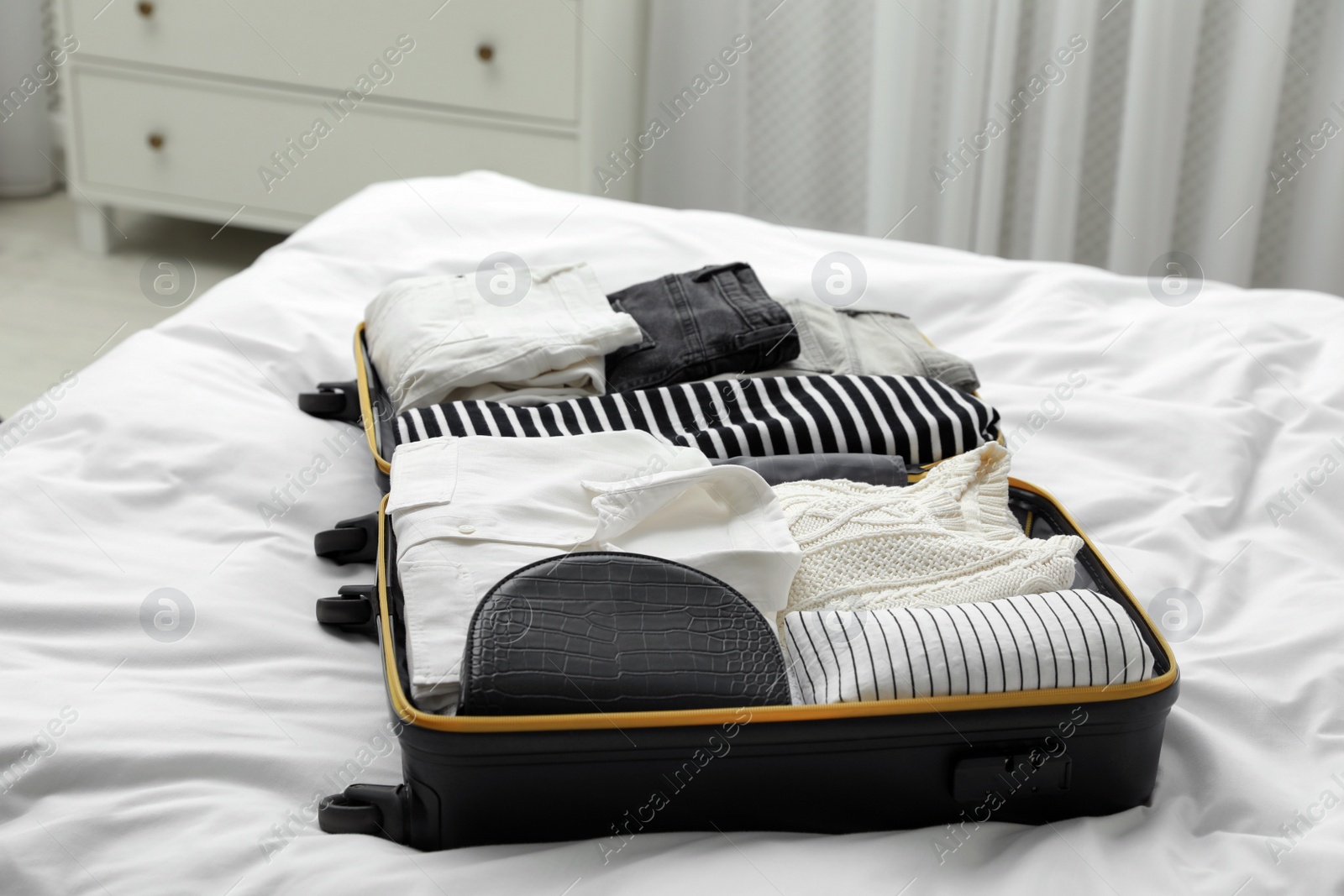 Photo of Open suitcase with clothes on bed indoors