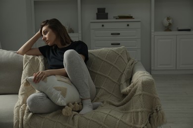 Sad young woman sitting on sofa at home, space for text