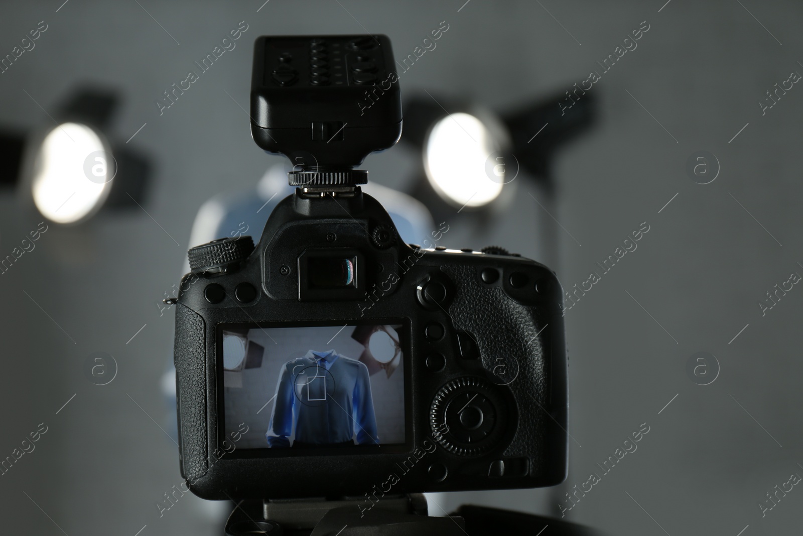 Photo of Ghost mannequin with stylish clothes and professional lighting equipment in modern studio, focus on camera. Fashion photography