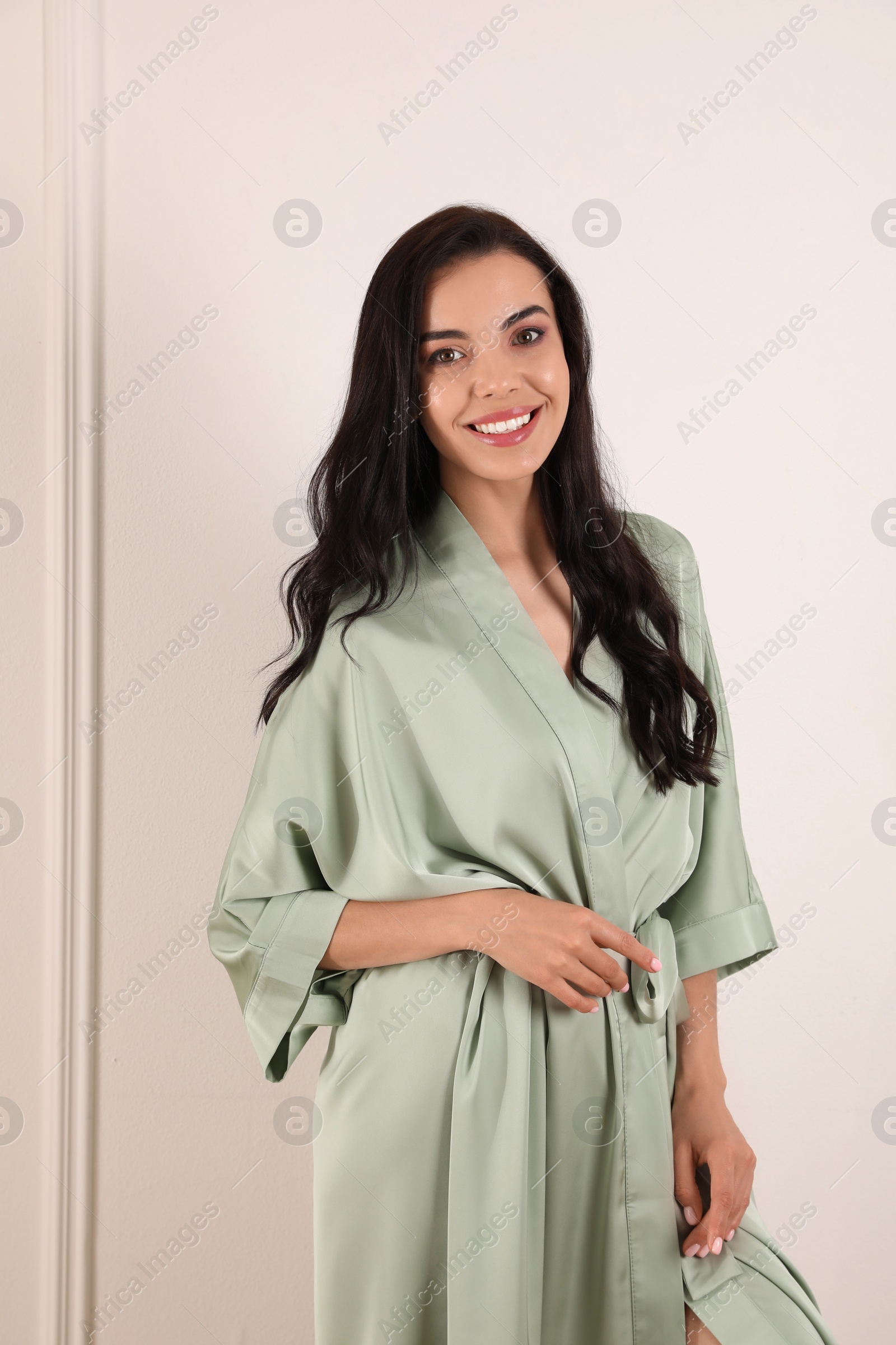 Photo of Pretty young woman in beautiful light silk robe near white wall