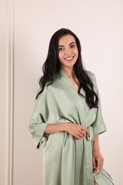 Photo of Pretty young woman in beautiful light silk robe near white wall