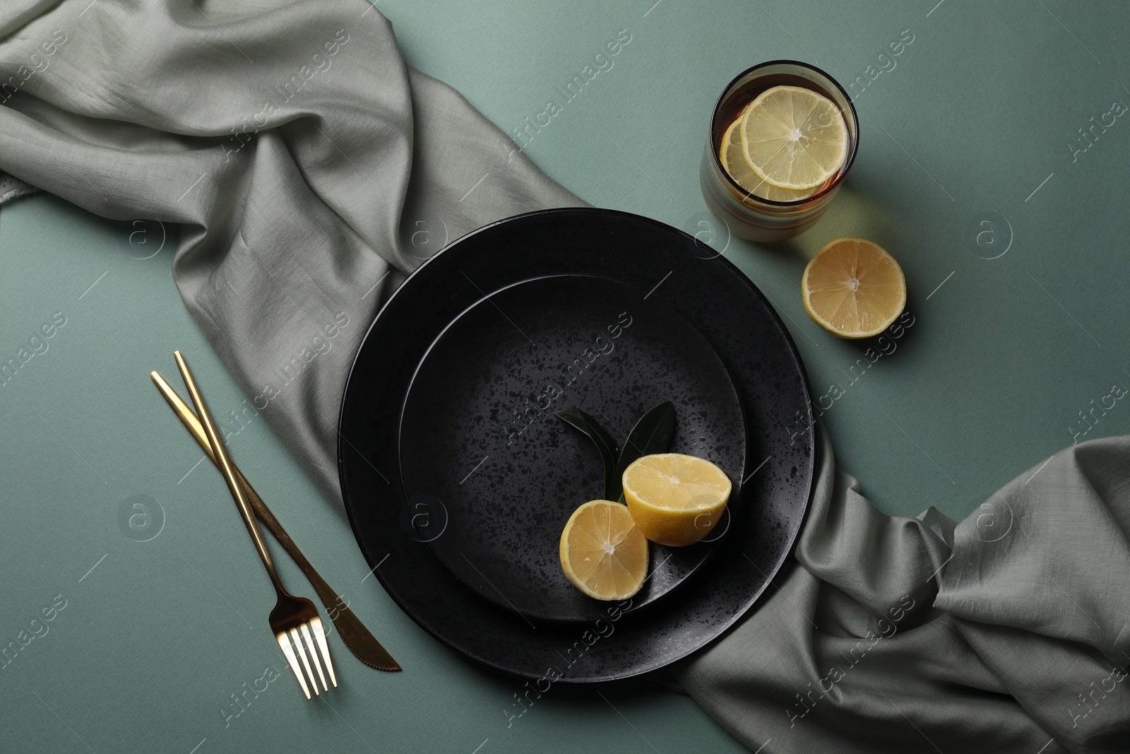 Photo of Stylish table setting. Plates, cutlery and tea with lemon on olive background, flat lay