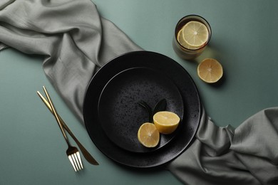 Stylish table setting. Plates, cutlery and tea with lemon on olive background, flat lay