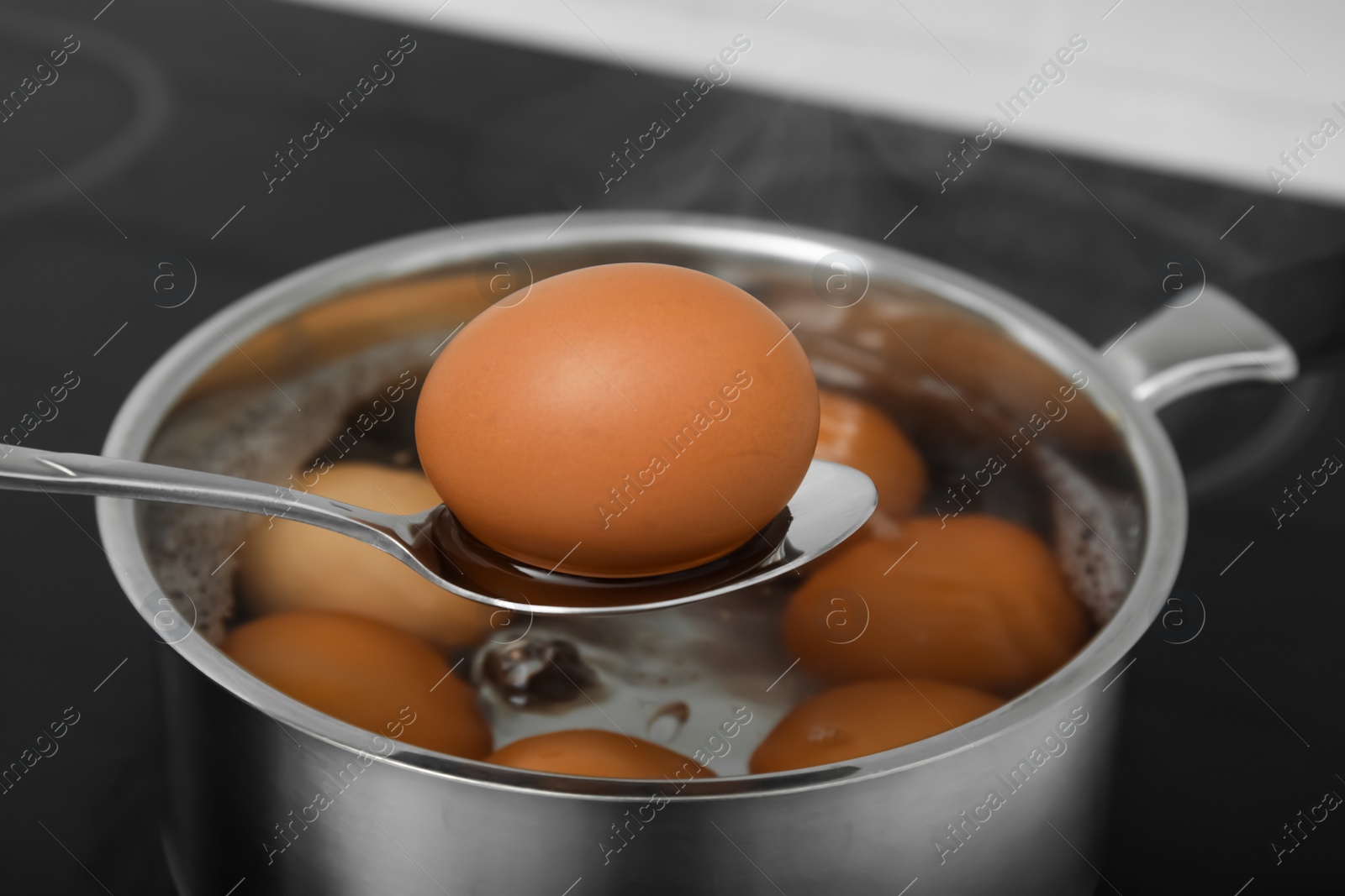 Photo of Spoon with boiled egg above saucepan on electric stove, closeup