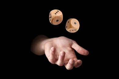 Image of Man throwing wooden dice on black background, closeup