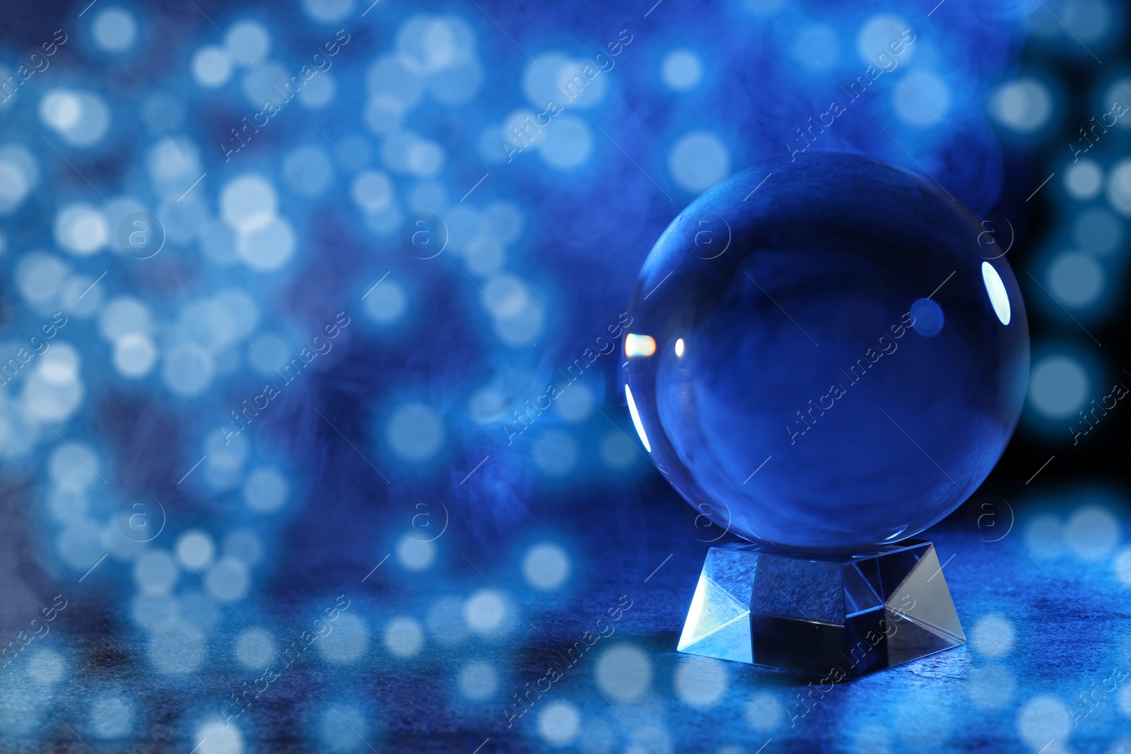 Photo of Magic crystal ball on table and smoke against dark background, space for text. Making predictions