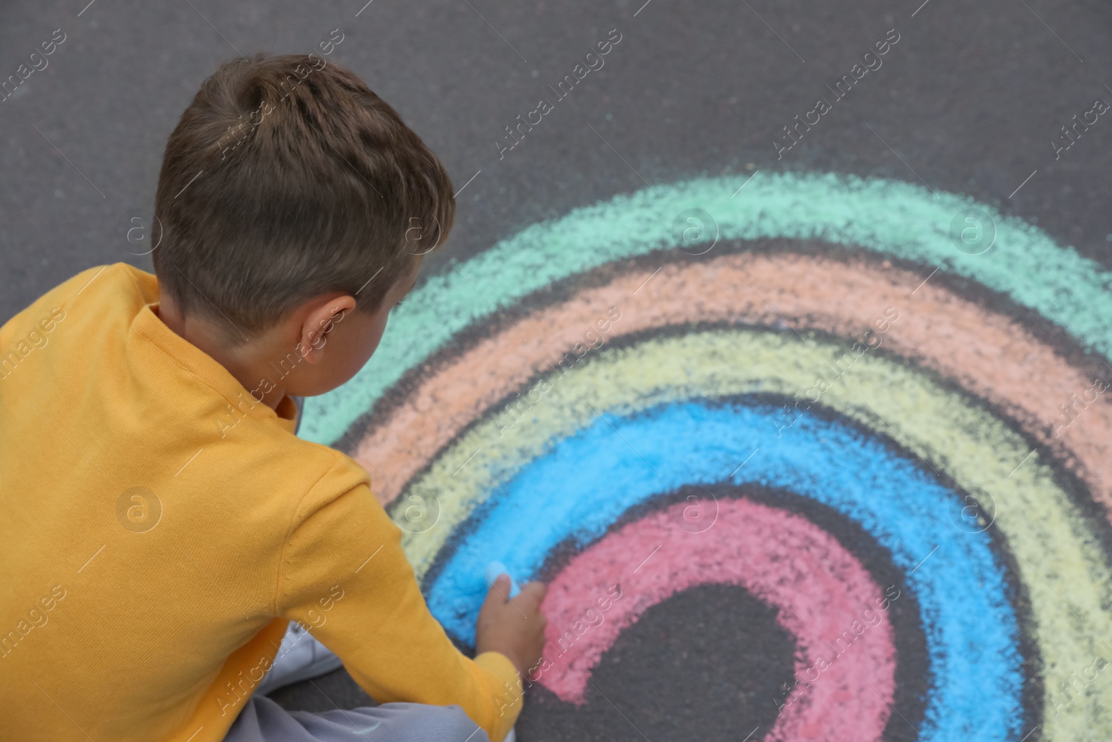 Photo of Child drawing rainbow with chalk on asphalt, above view