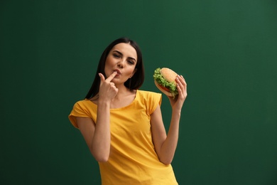 Young woman eating tasty burger on color background