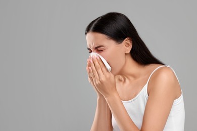 Photo of Suffering from allergy. Young woman blowing her nose in tissue on light grey background. Space for text