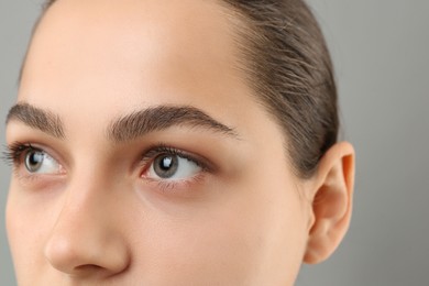 Young woman with perfect eyebrows on grey background, closeup