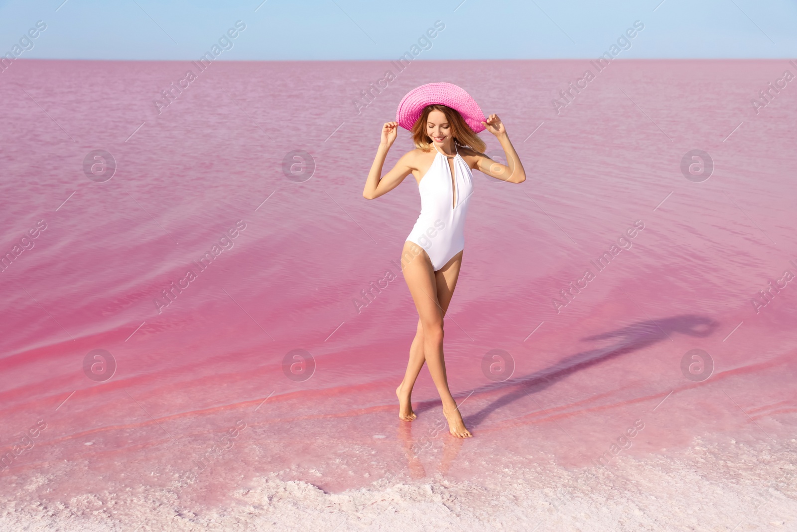 Photo of Beautiful woman in swimsuit posing near pink lake on sunny day