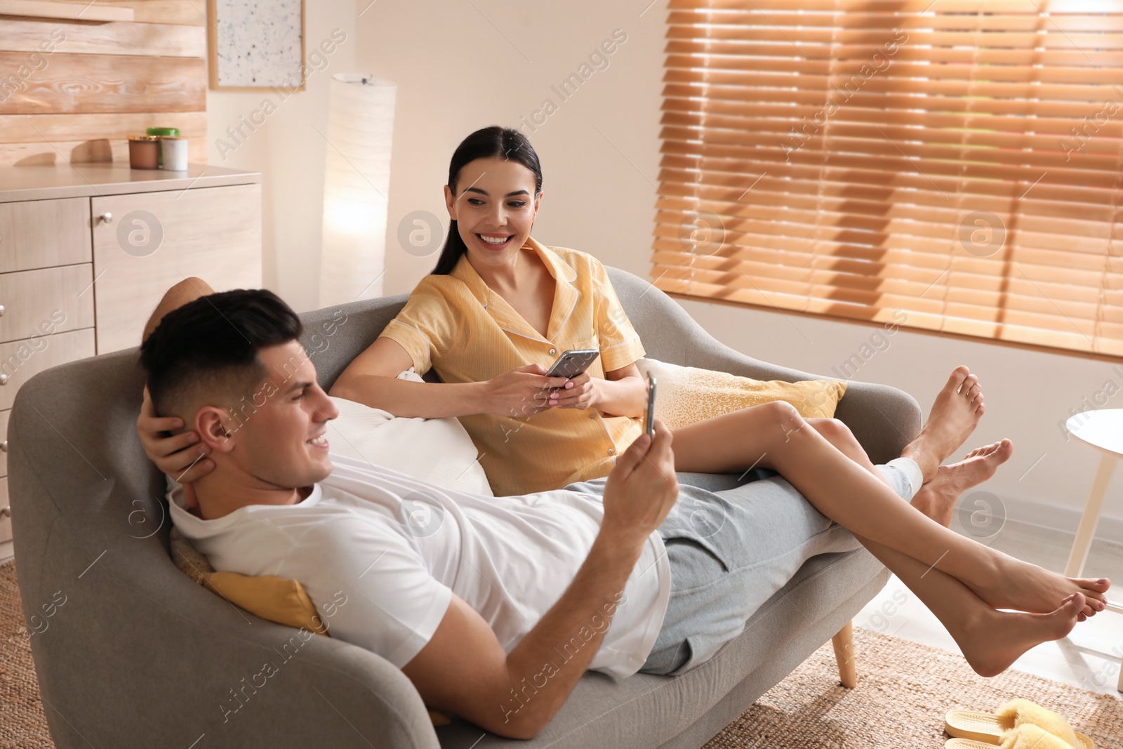 Photo of Happy couple in pyjamas with gadgets spending time together on sofa at home