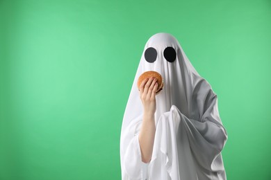 Creepy ghost. Person in white sheet with tasty hamburger on green background, space for text