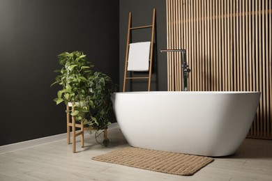 Spa day. Stylish bathroom interior with ceramic tub and green houseplants