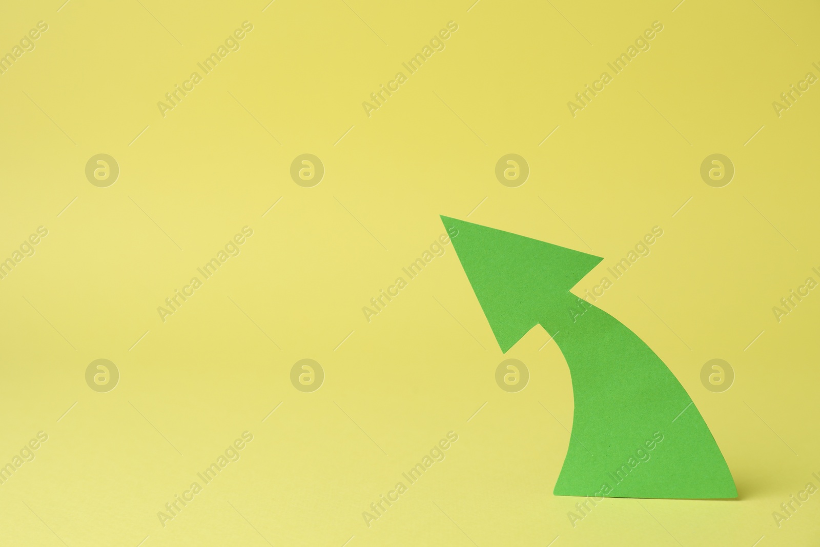 Photo of Curved green paper arrow on yellow background. Space for text