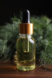 Photo of Bottle of essential oil and fresh dill on wooden table