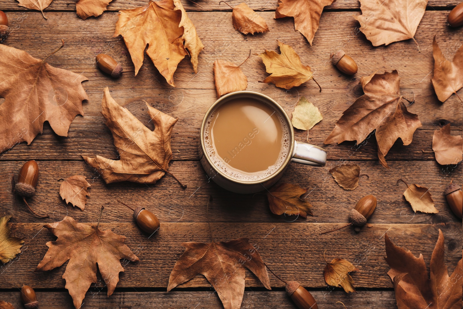 Photo of Cup of hot drink and autumn leaves on wooden table, flat lay. Cozy atmosphere