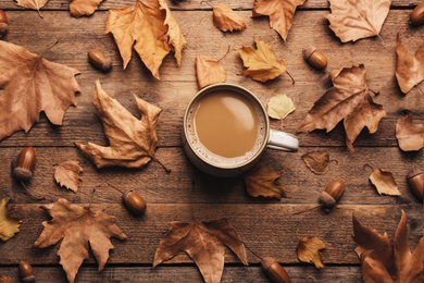 Cup of hot drink and autumn leaves on wooden table, flat lay. Cozy atmosphere