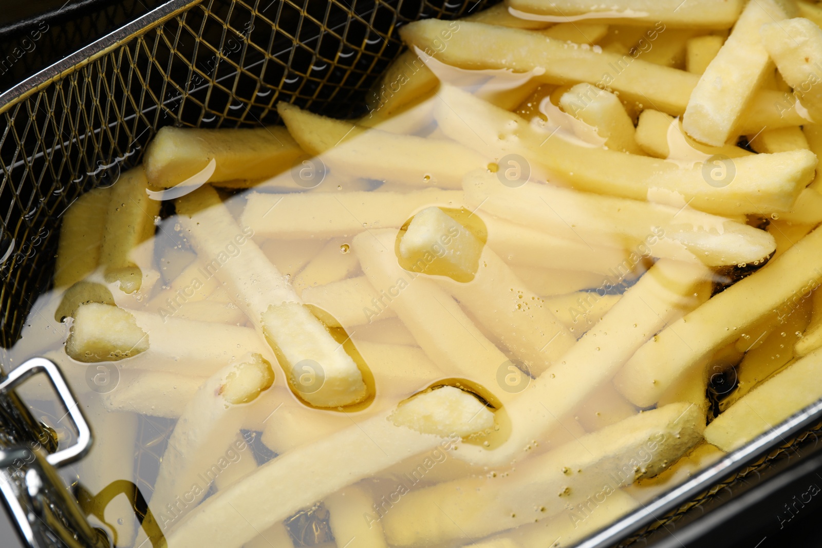 Photo of Cooking delicious french fries in hot oil, closeup