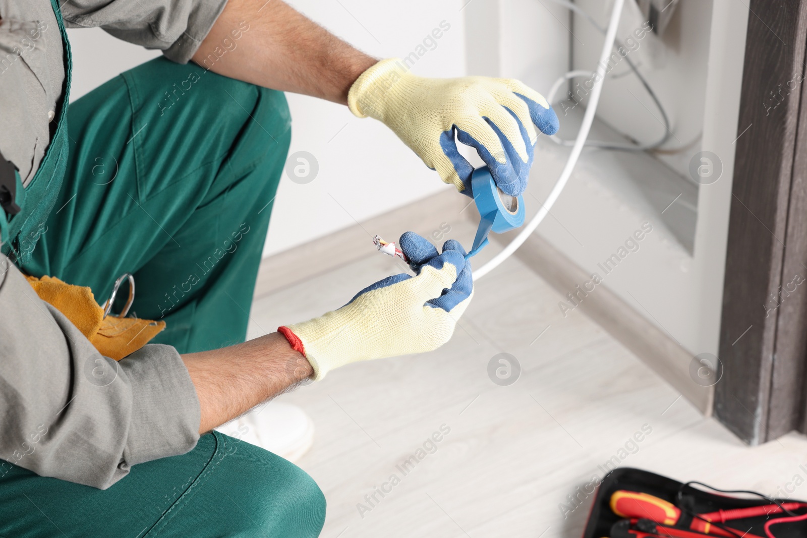 Photo of Electrician fixing wires with insulating tape indoors, closeup