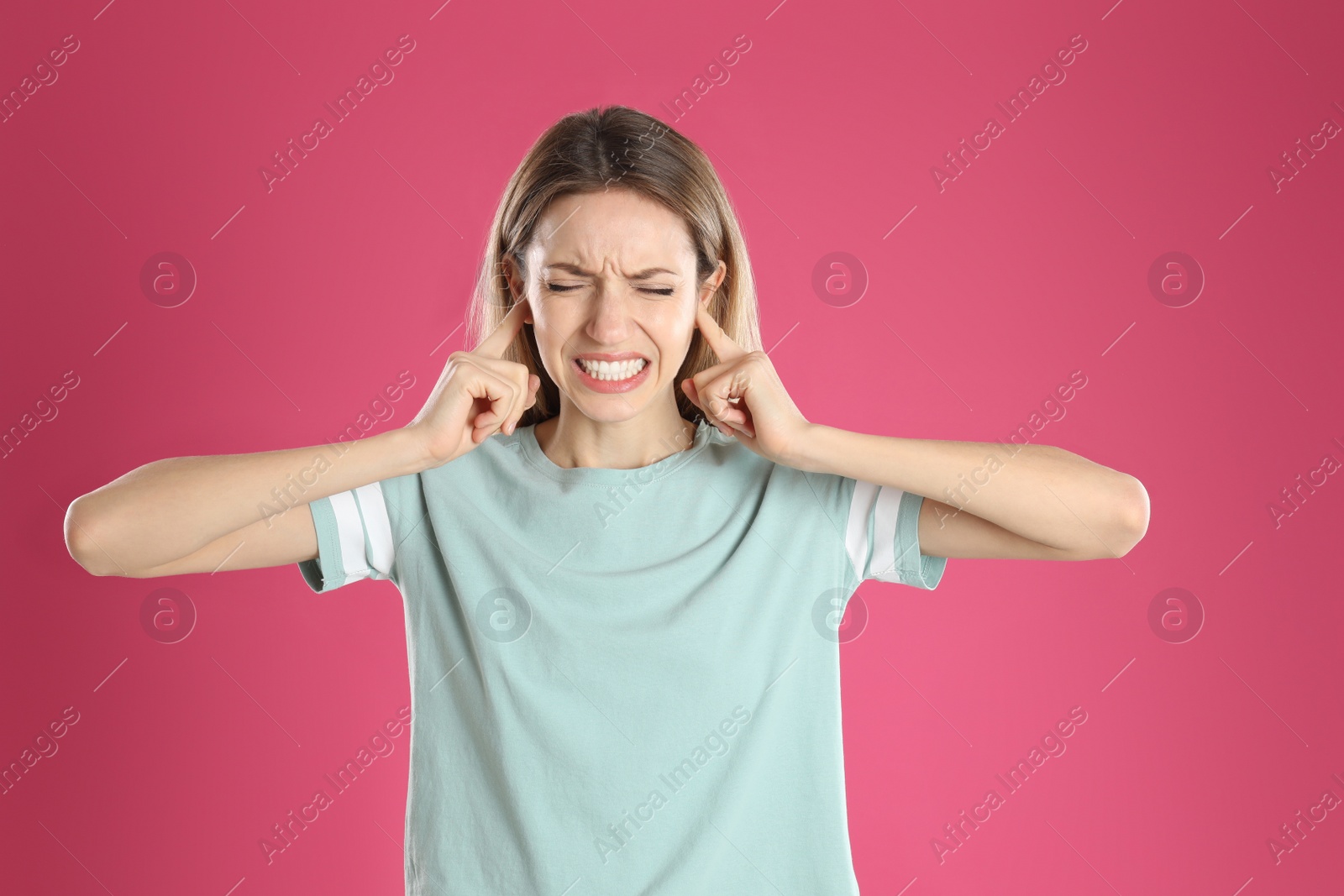 Photo of Emotional young woman covering her ears with fingers on pink background