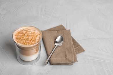 Glass with caramel macchiato, spoon and napkin on grey table