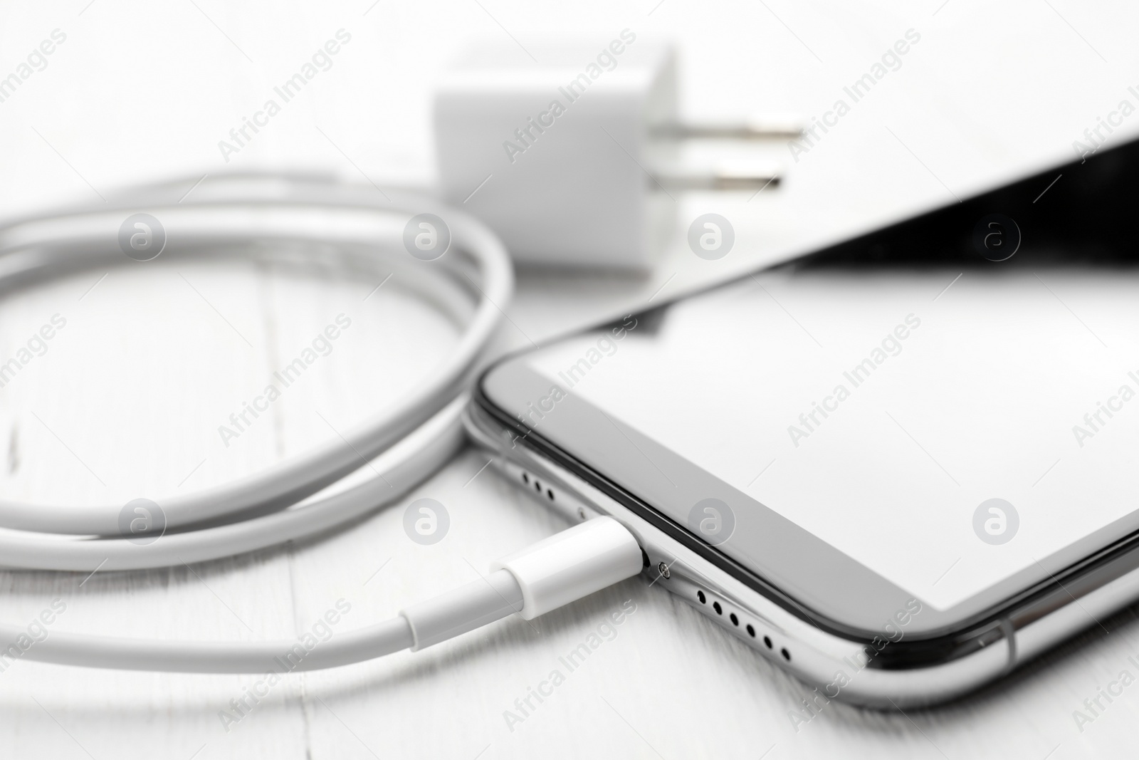 Photo of Smartphone and USB charger on white wooden table, closeup. Modern technology