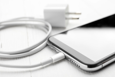 Smartphone and USB charger on white wooden table, closeup. Modern technology