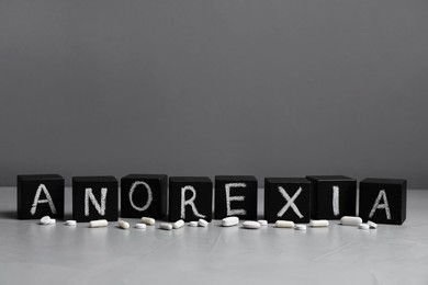 Photo of Word Anorexia made of cubes with chalked letters near pills on light table
