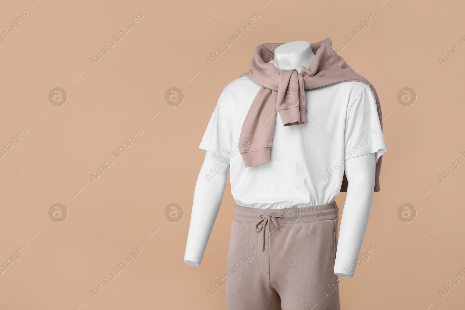 Photo of Male mannequin dressed in white t-shirt, sweater and pants on beige background, space for text