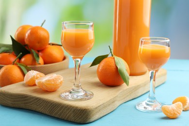 Photo of Delicious tangerine liqueur and fresh fruits on light blue wooden table
