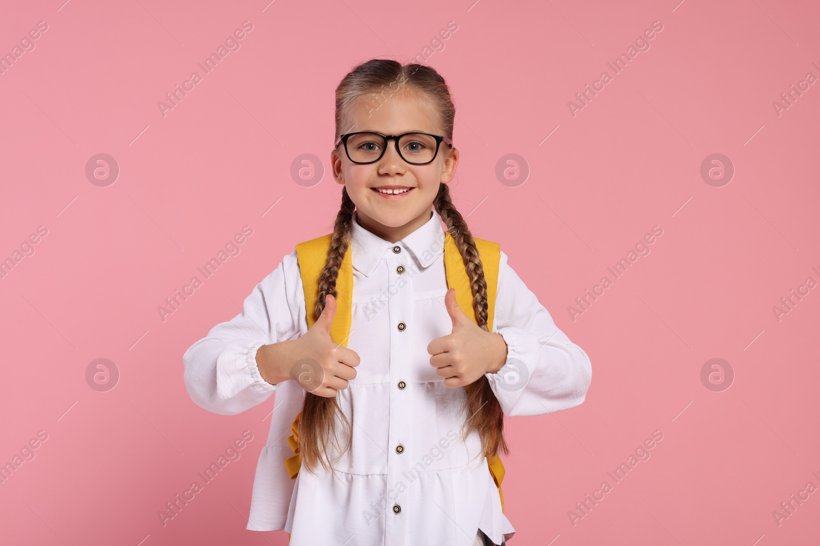 Photo of Happy schoolgirl with backpack showing thumbs up gesture on pink background