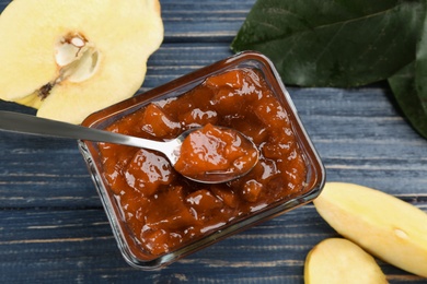 Delicious quince jam, fruits and leaves on blue wooden table, flat lay