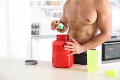 Photo of Young shirtless athletic man preparing protein shake in kitchen, closeup view. Space for text