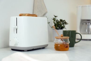 Photo of Modern toaster with bread slices and honey on white table in kitchen