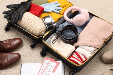 Photo of Open suitcase with warm clothes, accessories and shoes on floor