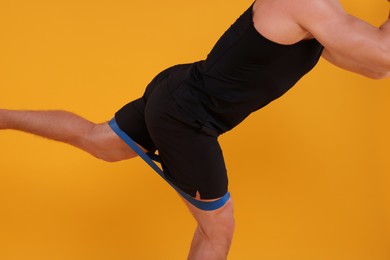 Young man exercising with elastic resistance band on orange background, closeup