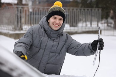 Photo of Man cleaning snow from car with brush outdoors