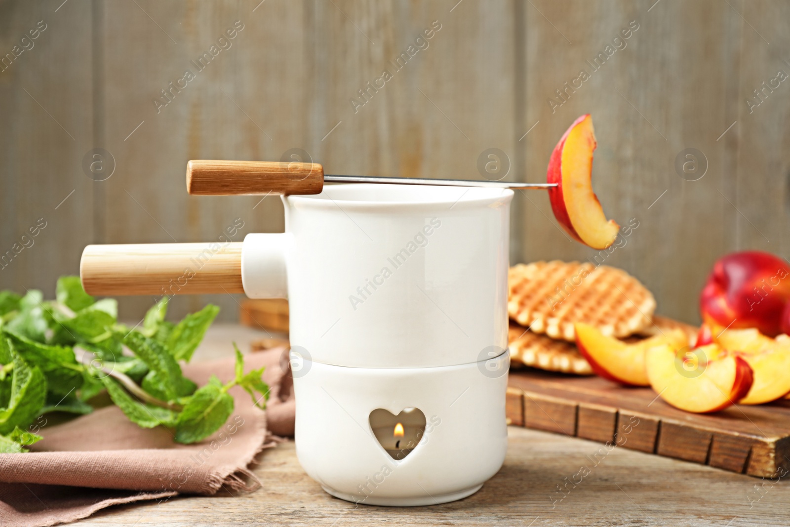 Photo of Fondue pot with chocolate and peaches on wooden table