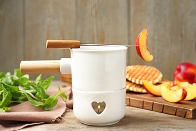 Photo of Fondue pot with chocolate and peaches on wooden table