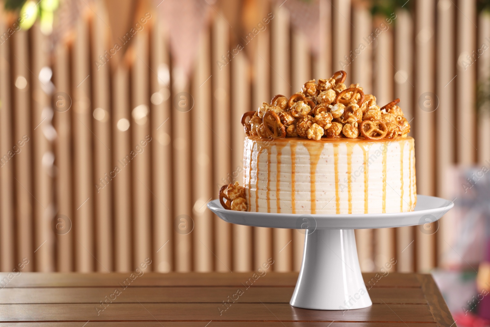 Photo of Caramel drip cake decorated with popcorn and pretzels on wooden table, space for text