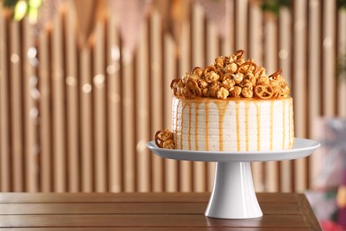 Caramel drip cake decorated with popcorn and pretzels on wooden table, space for text