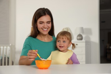 Photo of Mother feeding her cute little child with yogurt at white table in room