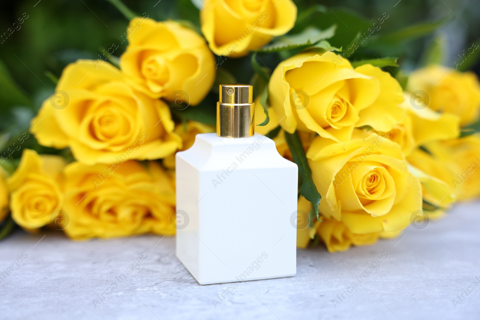 Photo of Perfume and beautiful bouquet of yellow roses on light table, closeup