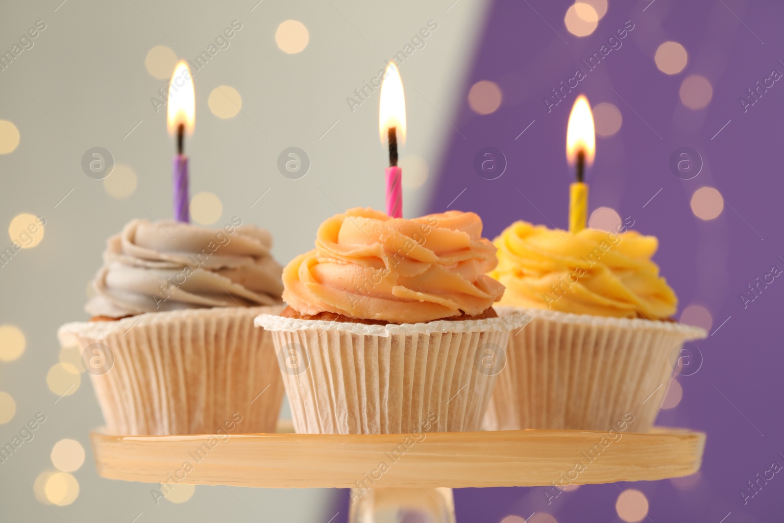 Photo of Tasty birthday cupcakes with candles on stand against blurred lights, closeup