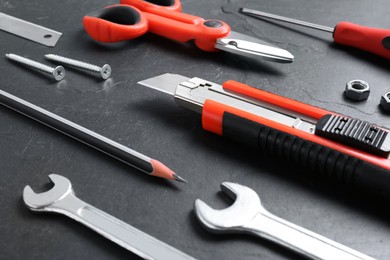 Photo of Utility knife and different tools on black table, closeup