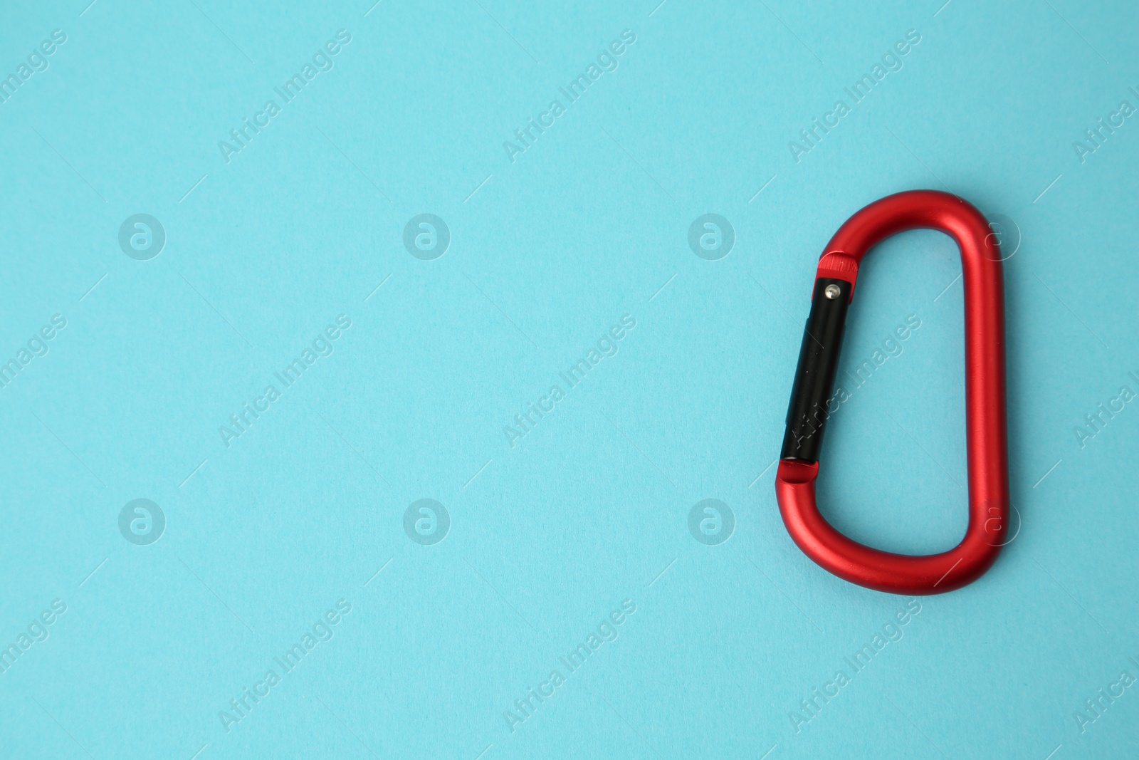 Photo of One red carabiner on light blue background, top view. Space for text