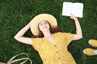 Young woman reading book on green grass, top view