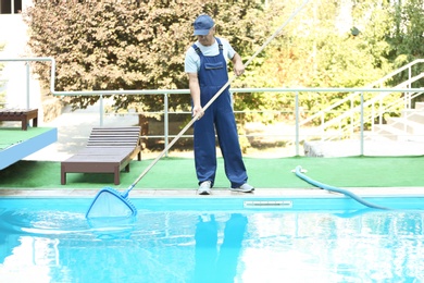 Photo of Male worker cleaning outdoor pool with scoop net